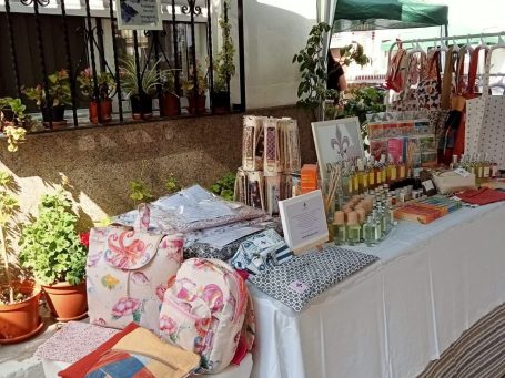 Mesa con productos artesanales y decorativos rodeada de plantas en macetas.