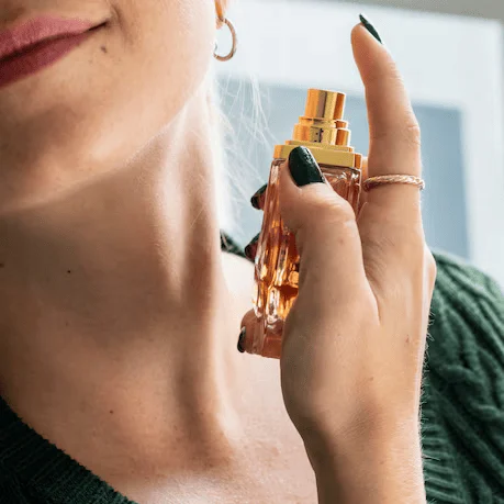 Mujer aplicando perfume, usando anillo y con uñas pintadas de negro.